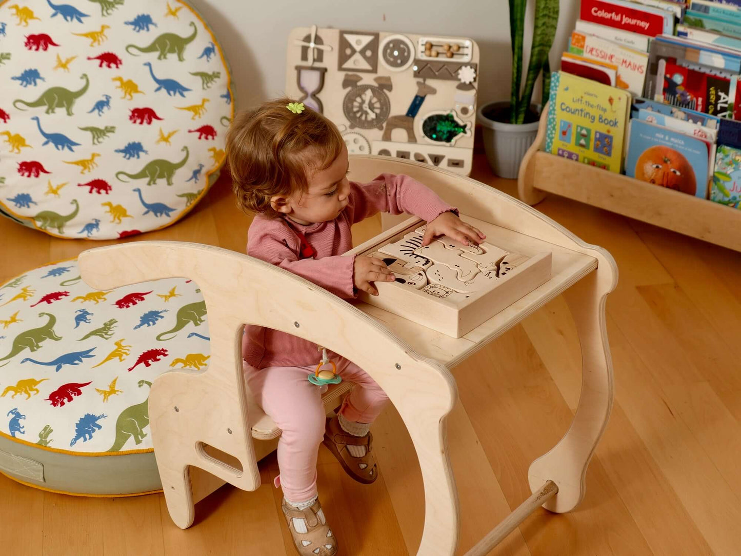 Toddler engaged with a Montessori-inspired wooden puzzle at a learning table, surrounded by colorful cushions.